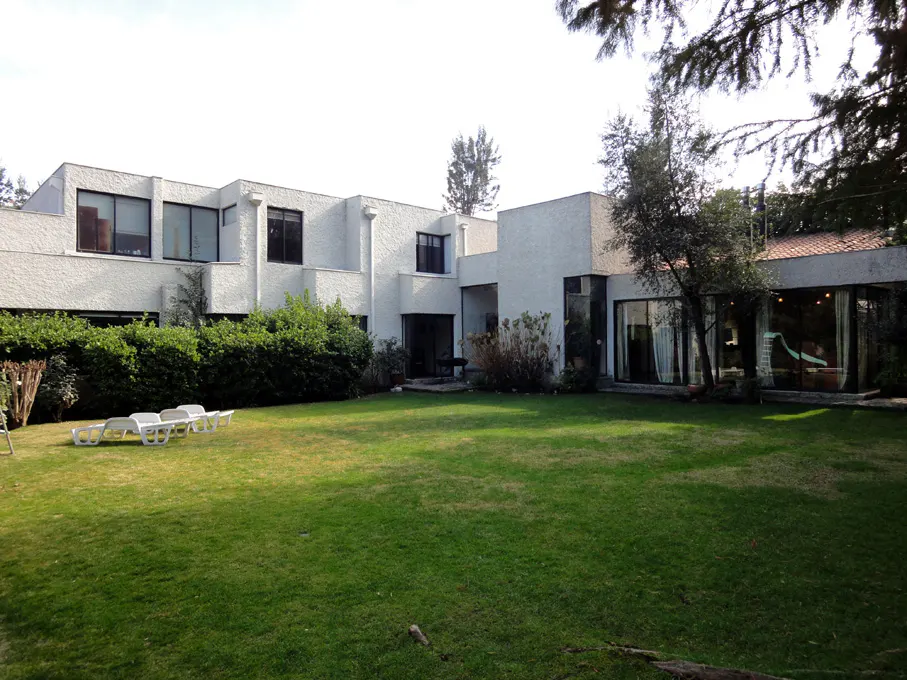 A modern white house with a large green lawn and white lounge chairs.