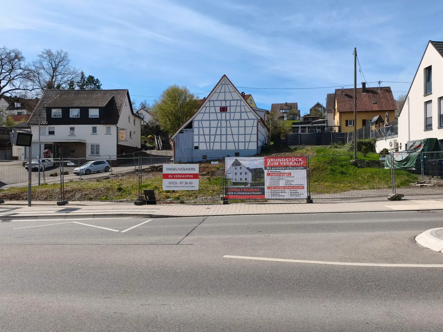 View of a street with "For Sale" signs in front of a vacant lot, with houses in the background.