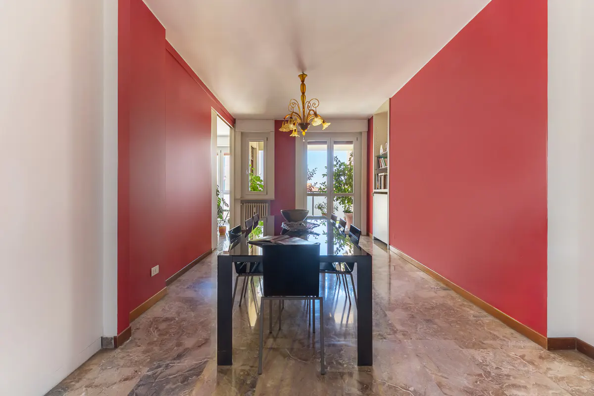 Dining room with red walls, marble floor, and a black table with chairs. A chandelier hangs above the table.