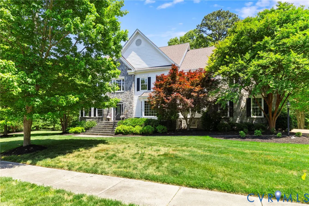 Two-story house with stone and white siding, black shutters, and a green lawn with trees.