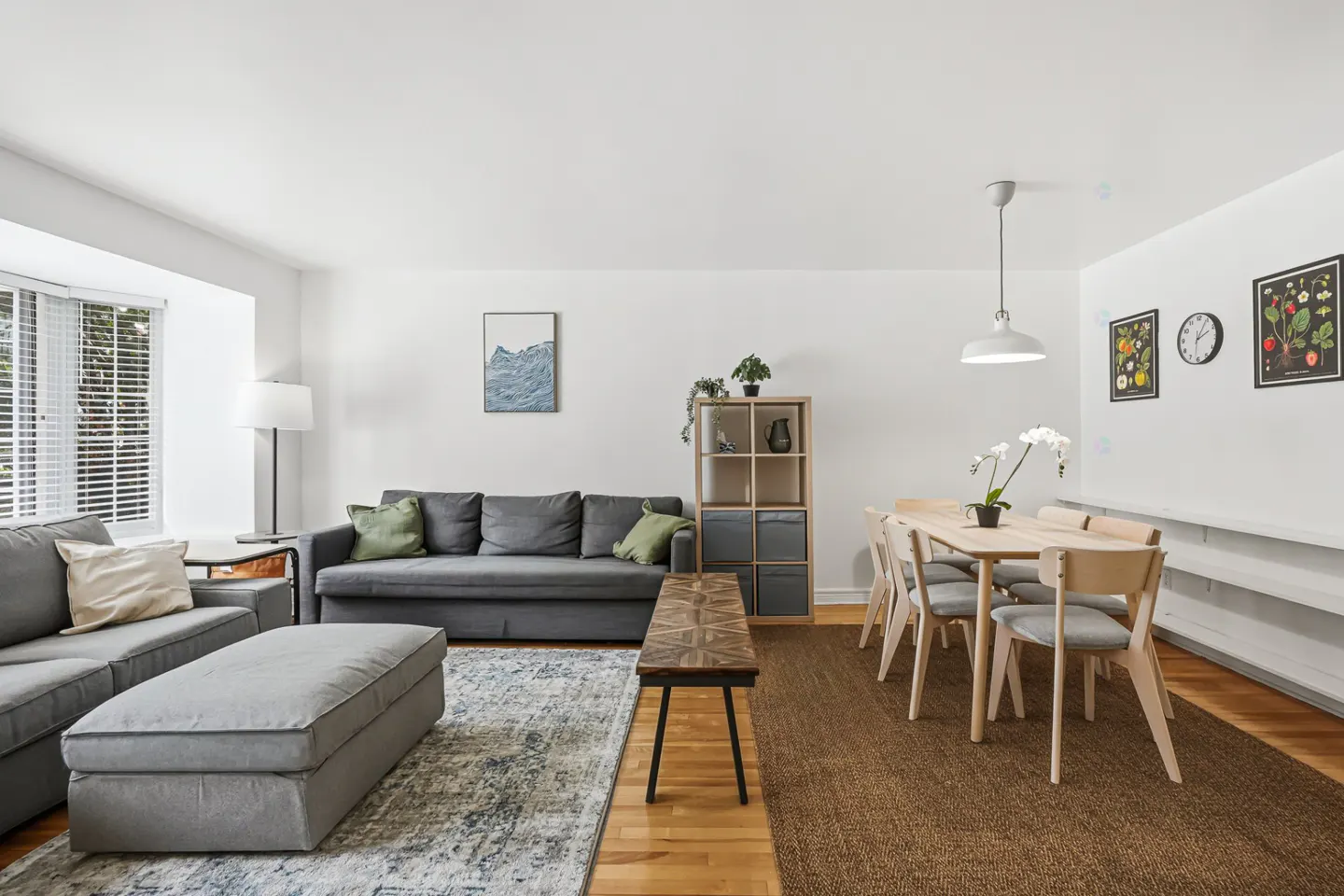 Bright living and dining area with gray sofas, wood floors, and a light wood dining table with six chairs.