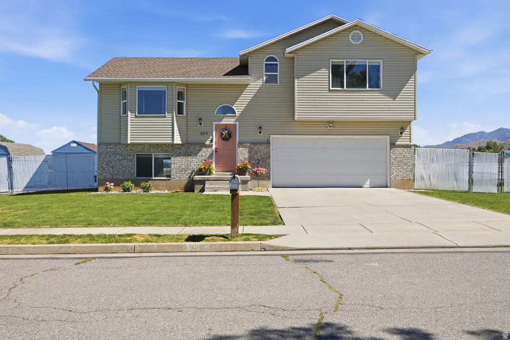 Two-story beige house with a stone base, white garage, pink front door, and green lawn under a clear blue sky.
