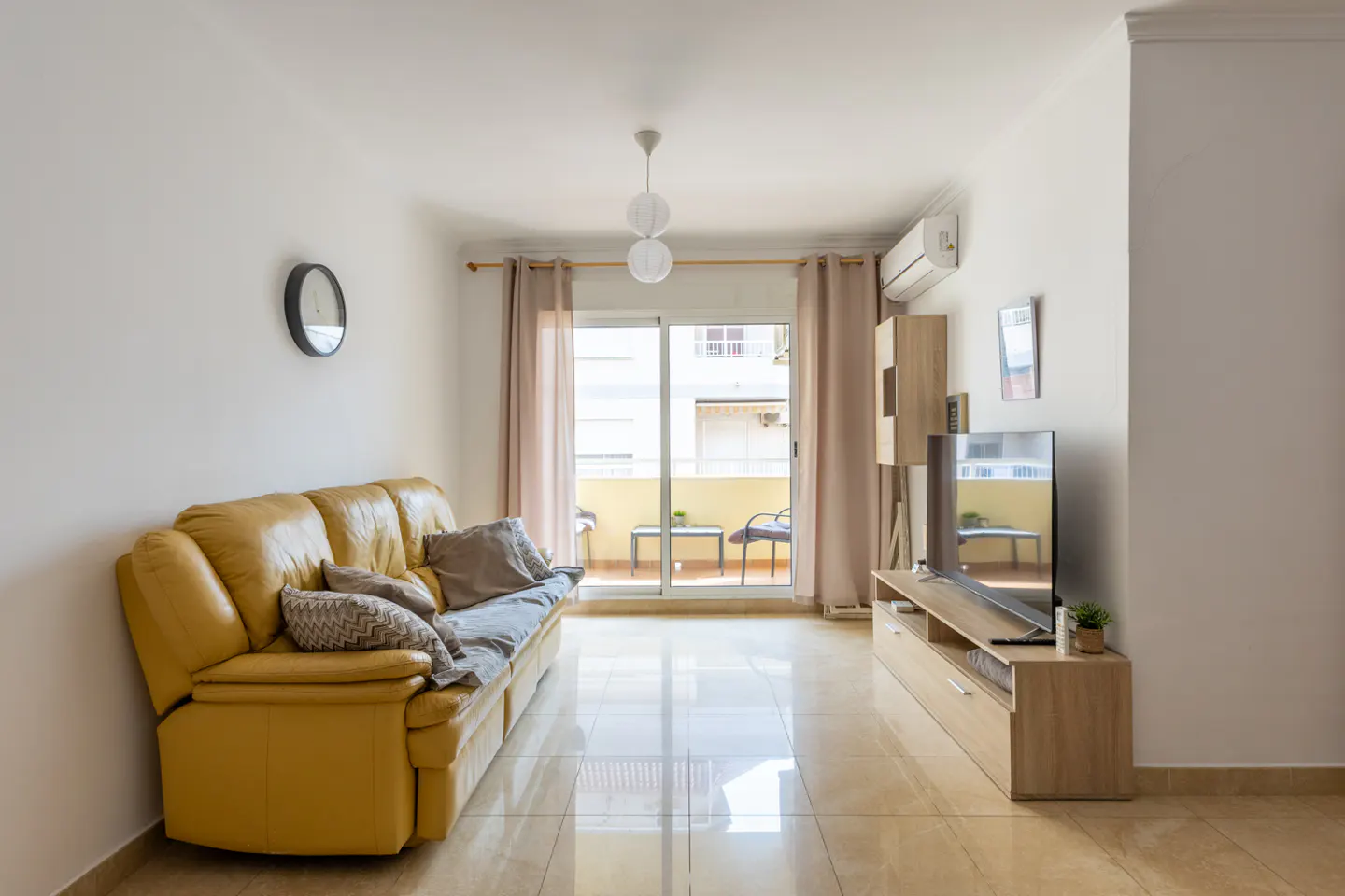 Bright living room with a yellow leather sofa, TV, and balcony with outdoor furniture.