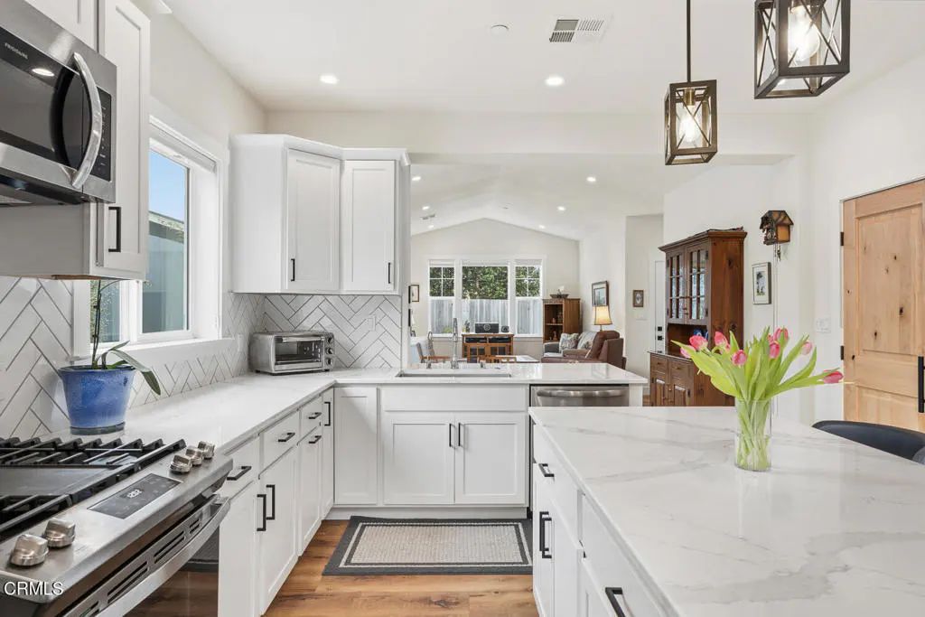 Modern white kitchen with marble countertops, herringbone backsplash, stainless appliances, and a vase of pink tulips.