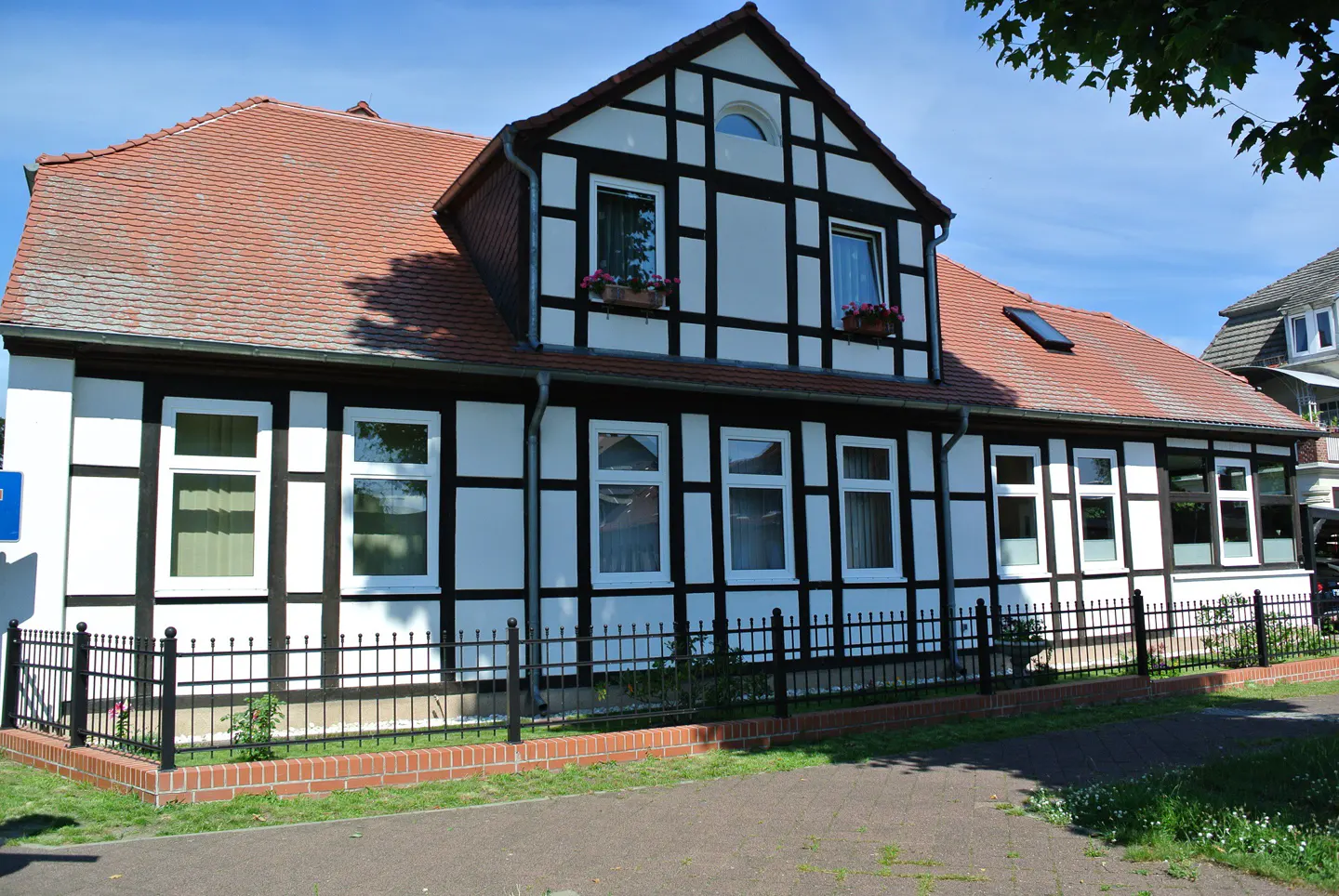 Two-story timber frame house with white walls, dark brown beams, and a red tile roof. Black metal fence in front.