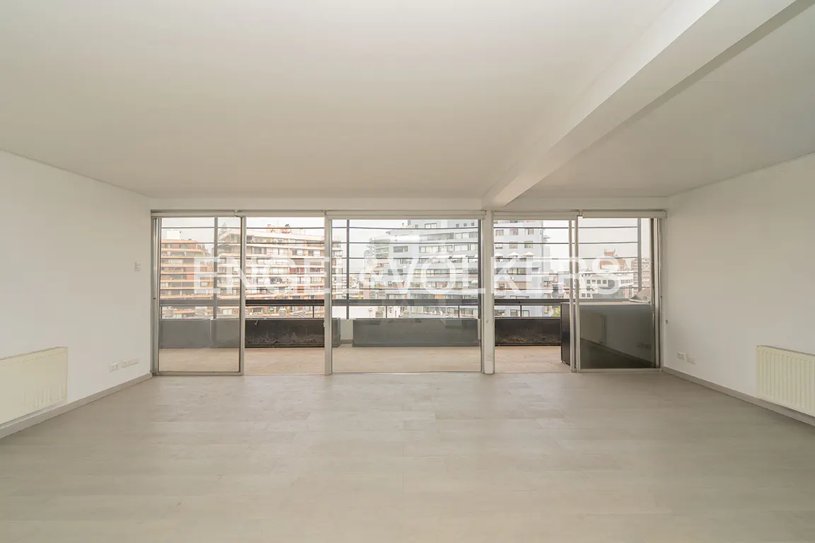 Empty, bright room with white walls, gray floor, and large sliding glass doors leading to a balcony with city views.
