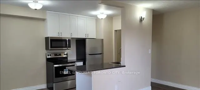 Modern kitchen with white cabinets, stainless steel appliances, and a breakfast bar opening to a neutral-toned living area.