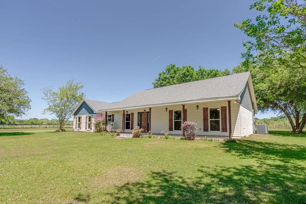 Single-story home with white siding, brown shutters, and a gray roof on a green lawn under a clear blue sky.