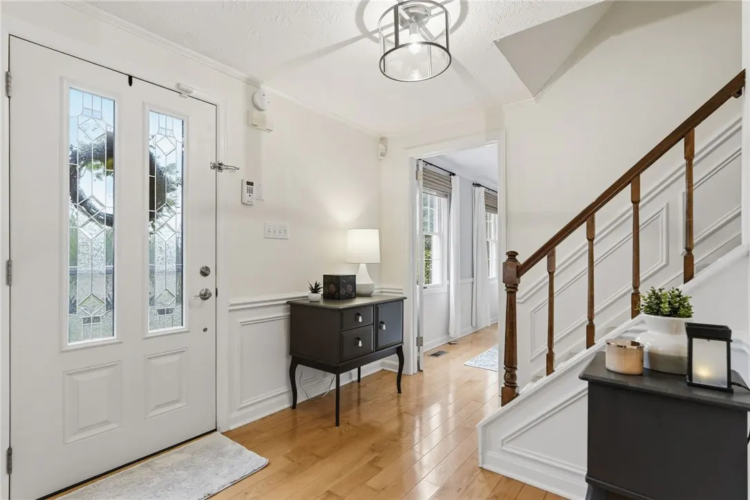 Bright foyer with wood floors, white walls, and a decorative glass front door. A dark wood console table sits near the stairs.