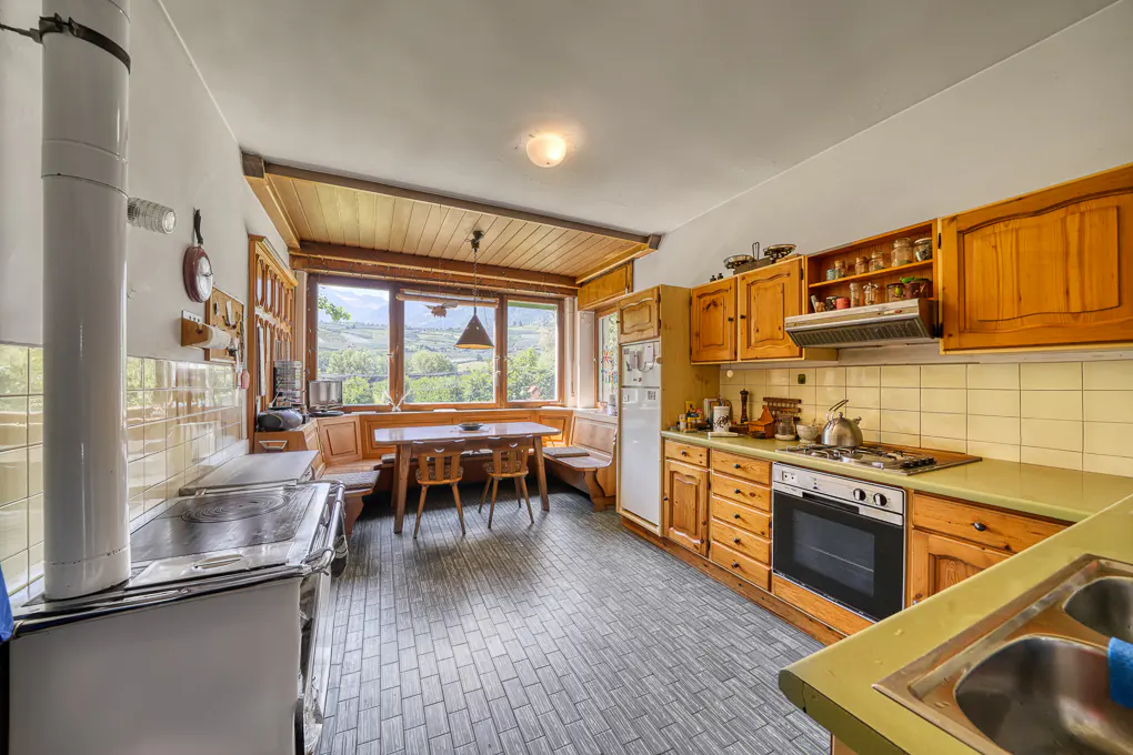 Rustic kitchen with wooden cabinets, a dining nook, and a large window overlooking a scenic mountain landscape.