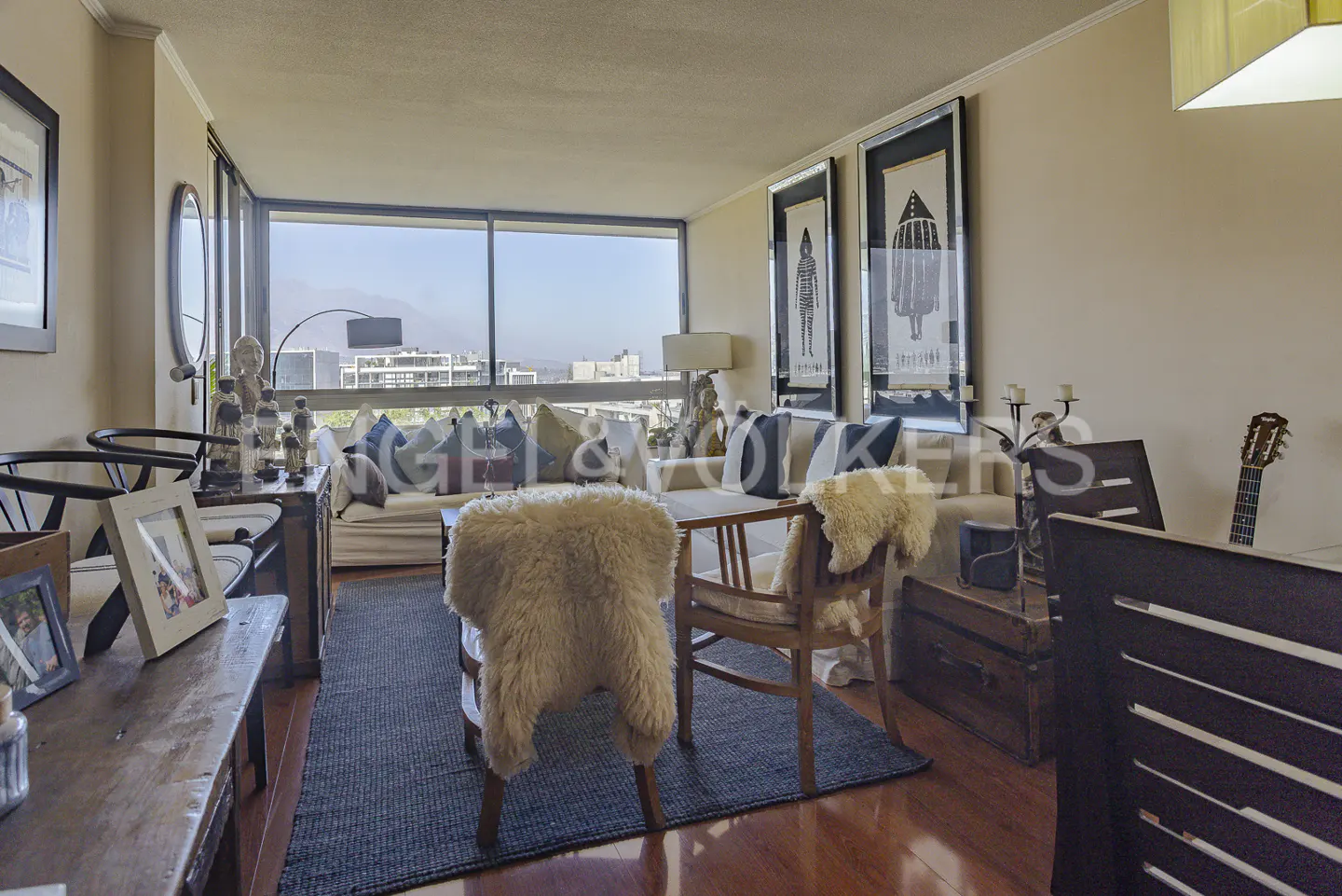 Living room with wood floors, a large window with a city view, and a sofa with decorative pillows. Two framed art pieces hang on the wall.