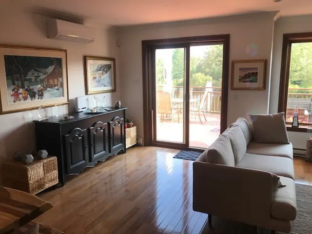 Living room with hardwood floors, a beige sofa, and a dark wood sideboard with framed art above. Sliding glass doors lead to a deck.