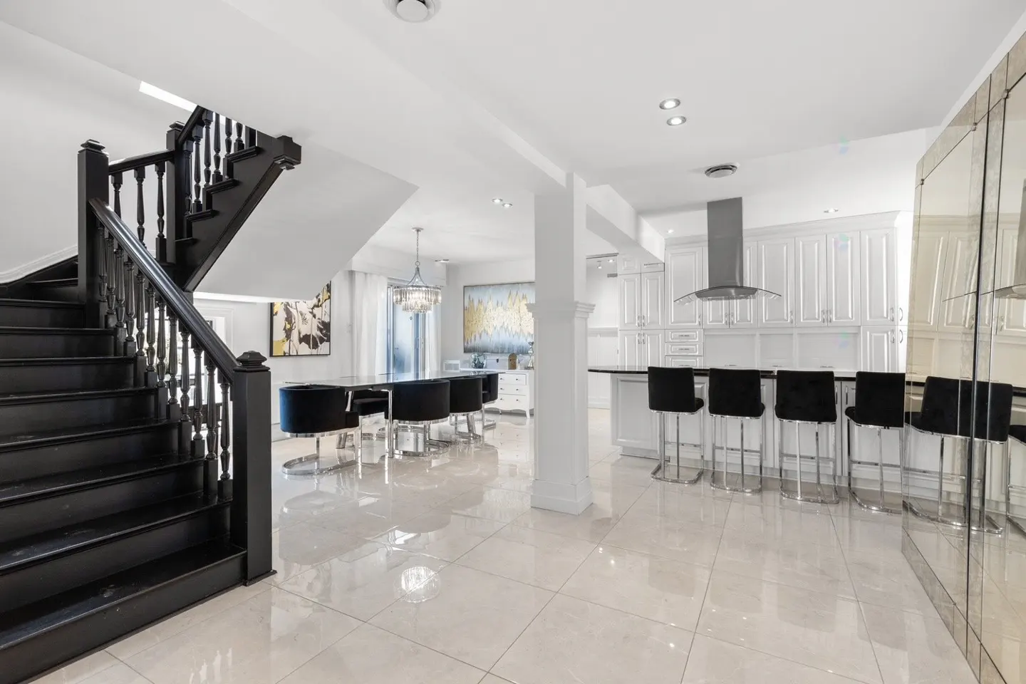 Open-concept home interior with black staircase, dining table with black chairs, and white kitchen with black bar stools.