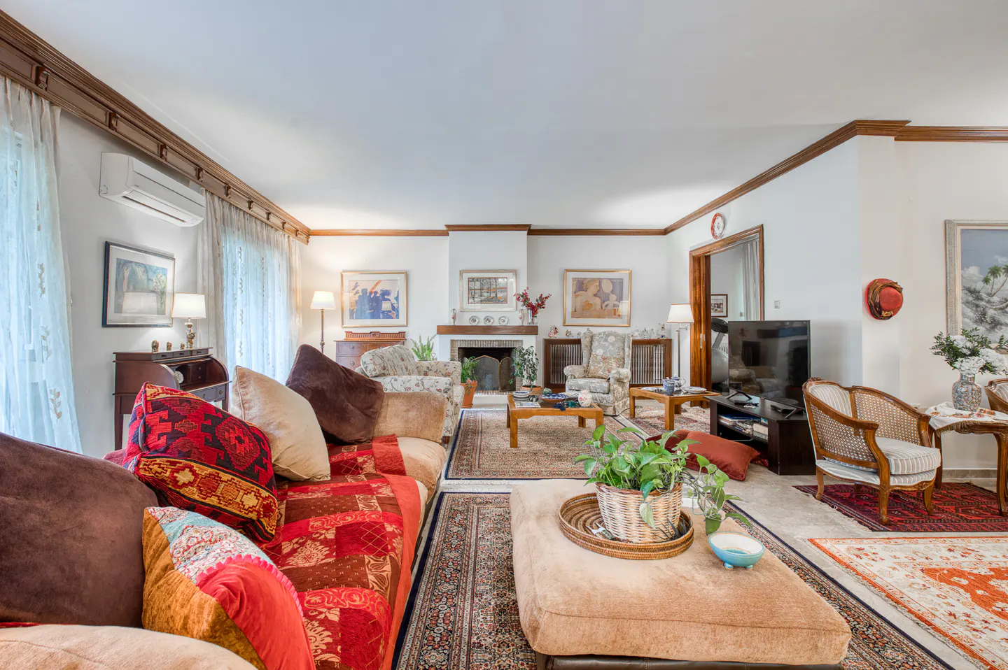 A living room with a fireplace, patterned rugs, and a brown couch with colorful pillows.