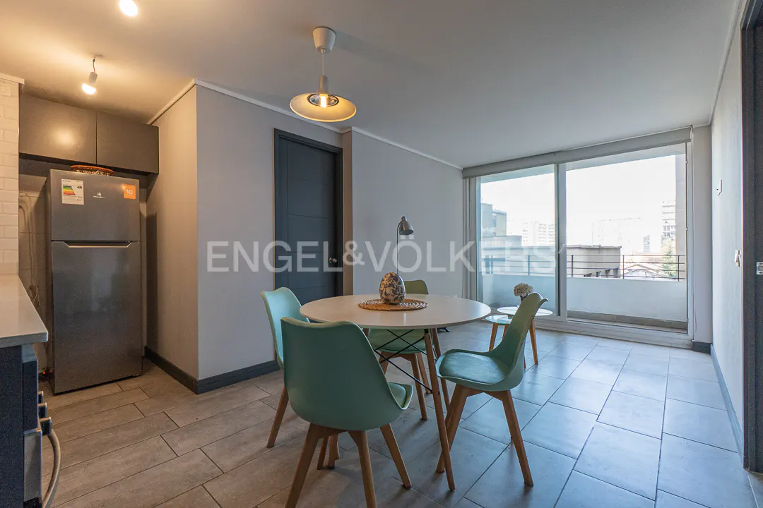 Modern dining area with a round white table, four light blue chairs, and a stainless steel refrigerator in the kitchen.