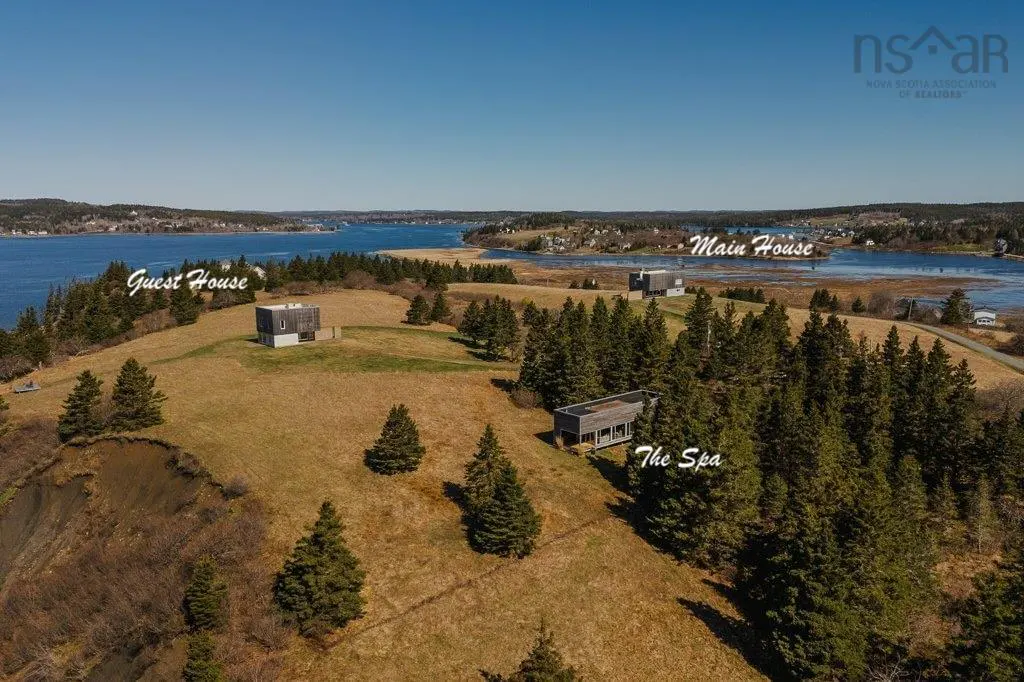 Aerial view of a property with a main house, guest house, and spa on a grassy peninsula surrounded by water.