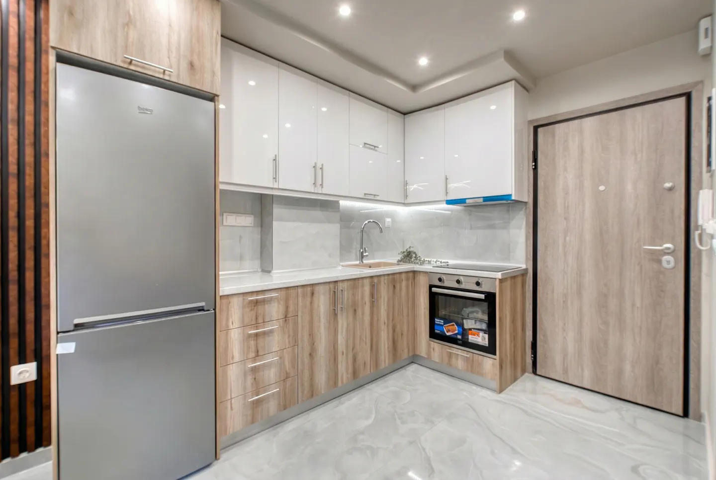 A modern kitchen with white cabinets, wood-grain lower cabinets, a stainless steel refrigerator, and a gray marble floor.