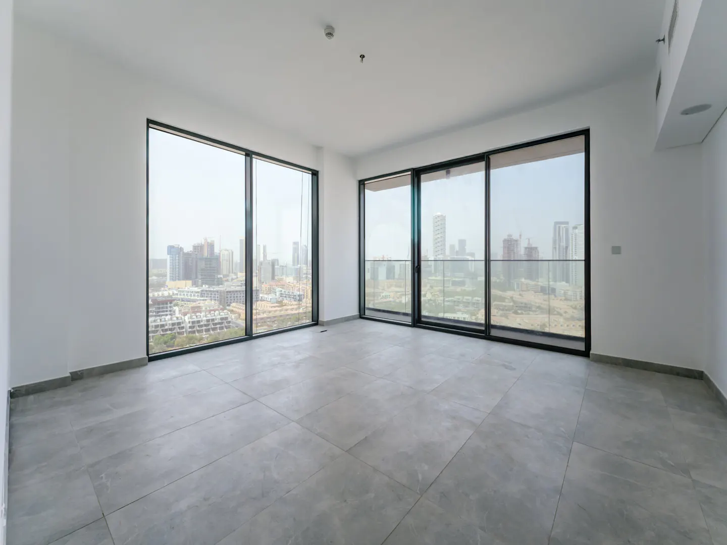 Empty room with gray tile floor, white walls, and large windows showing a city skyline.