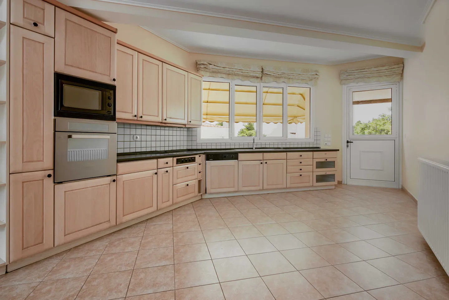 Spacious kitchen with light wood cabinets, black countertops, tiled backsplash, stainless appliances, and a glass door.