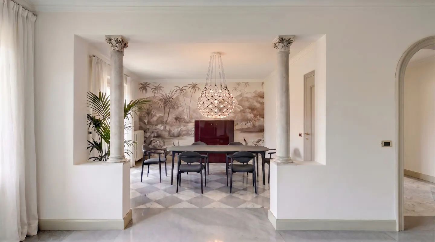 Dining room with marble floors, white walls, and columns framing a table with black chairs. A tropical mural and modern chandelier add style.