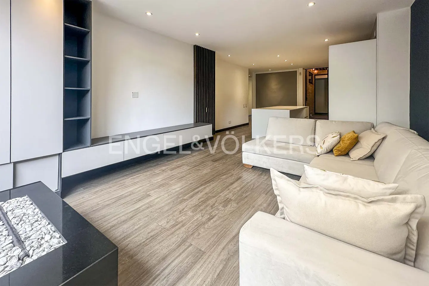 Living room with light wood floors, a white sectional sofa with pillows, and a gray built-in shelving unit.