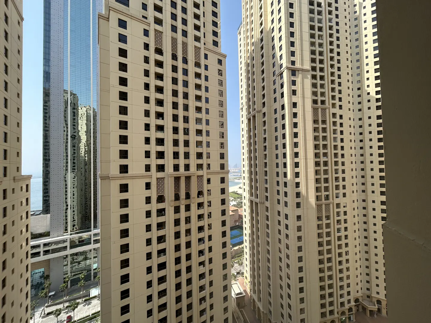 View of tall, beige apartment buildings with dark windows, and a blue glass skyscraper in the background.