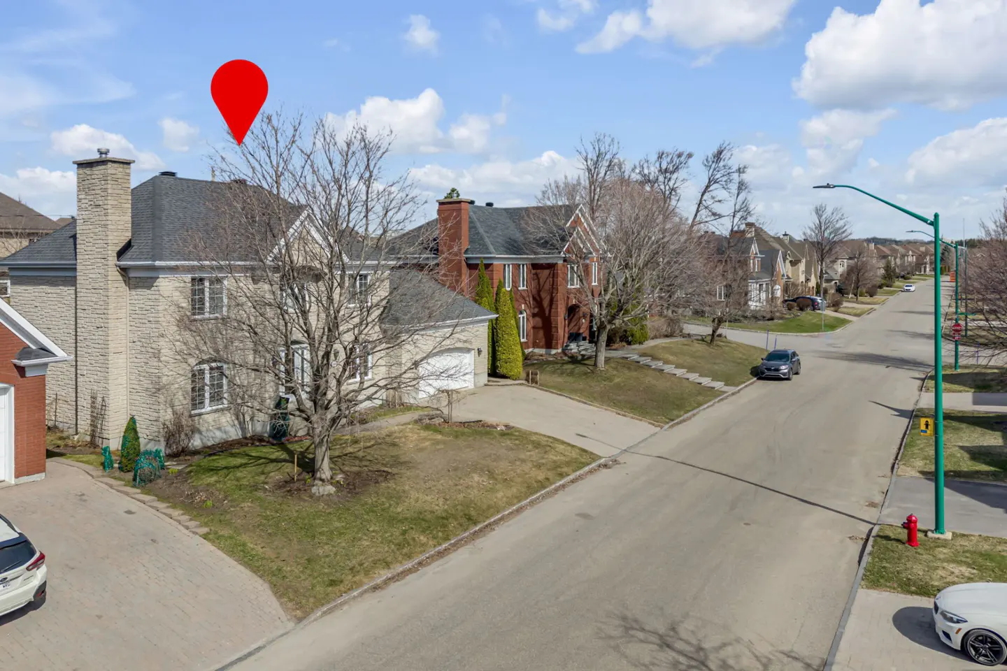 Exterior view of a two-story stone house with a red location pin above it, on a street with other houses.