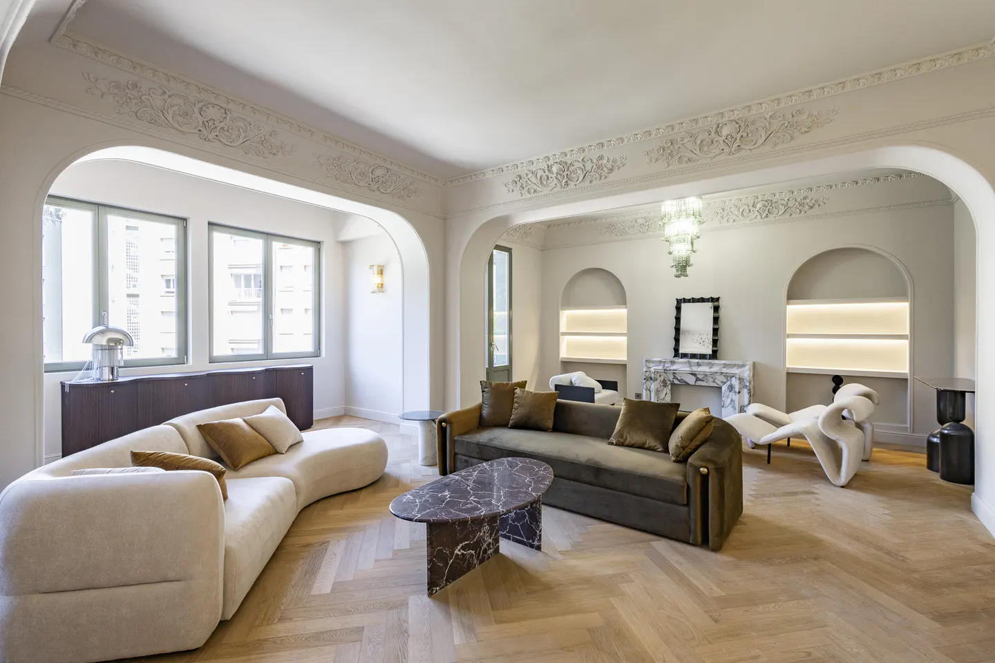 Bright living room with herringbone wood floors, arched doorways, and ornate ceiling trim. A cream sofa and olive sofa face each other.
