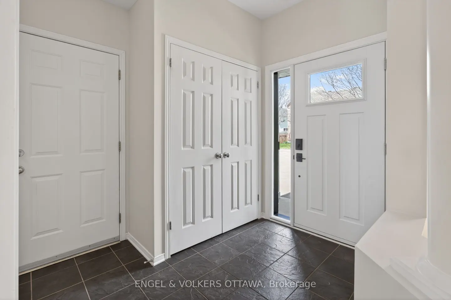 Entryway with white doors, dark tile floor, and neutral walls. A front door with a window is visible.
