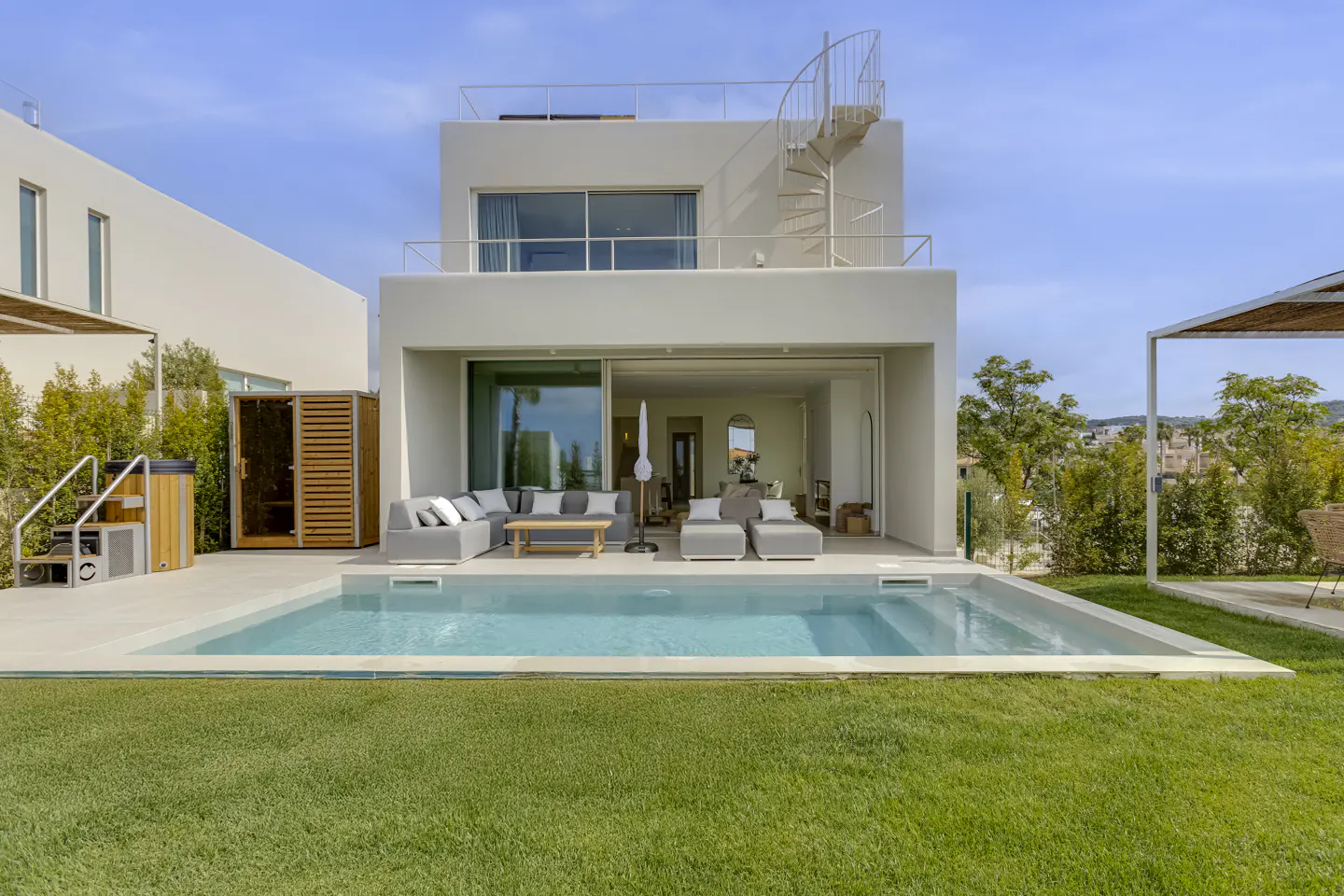 Modern white house with a pool, gray outdoor furniture, and a spiral staircase to the roof. Green lawn in the foreground.