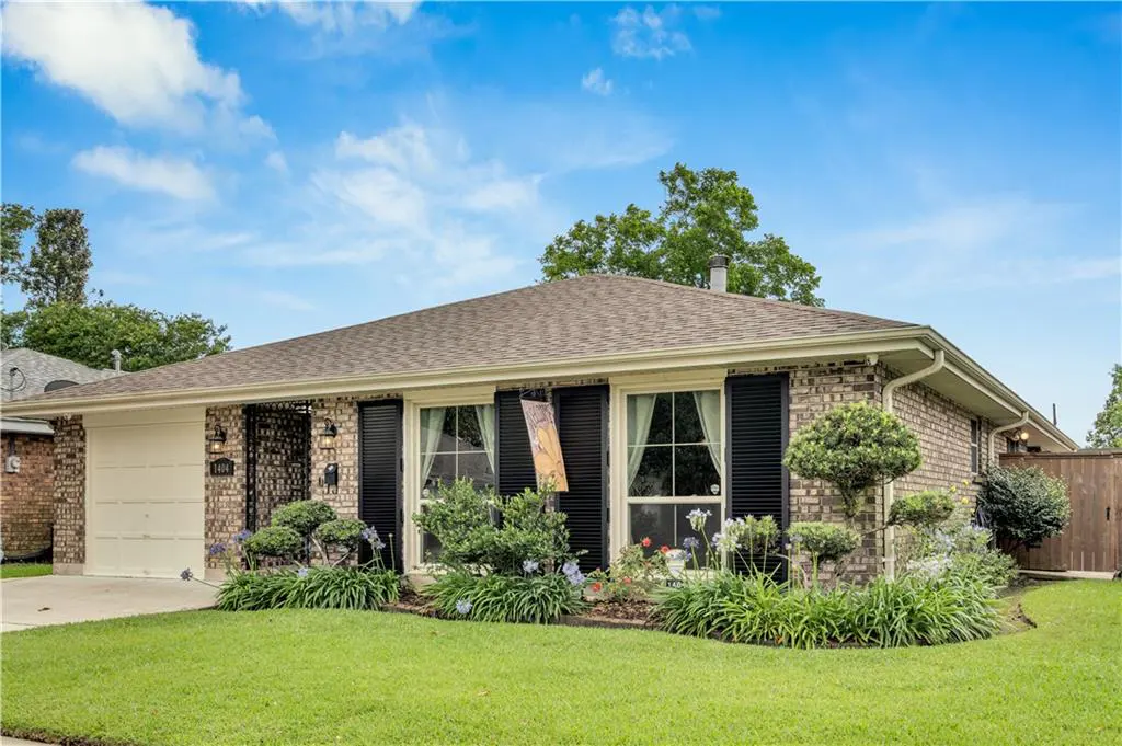 Single-story brick house with black shutters, a brown roof, and a green lawn under a blue sky.