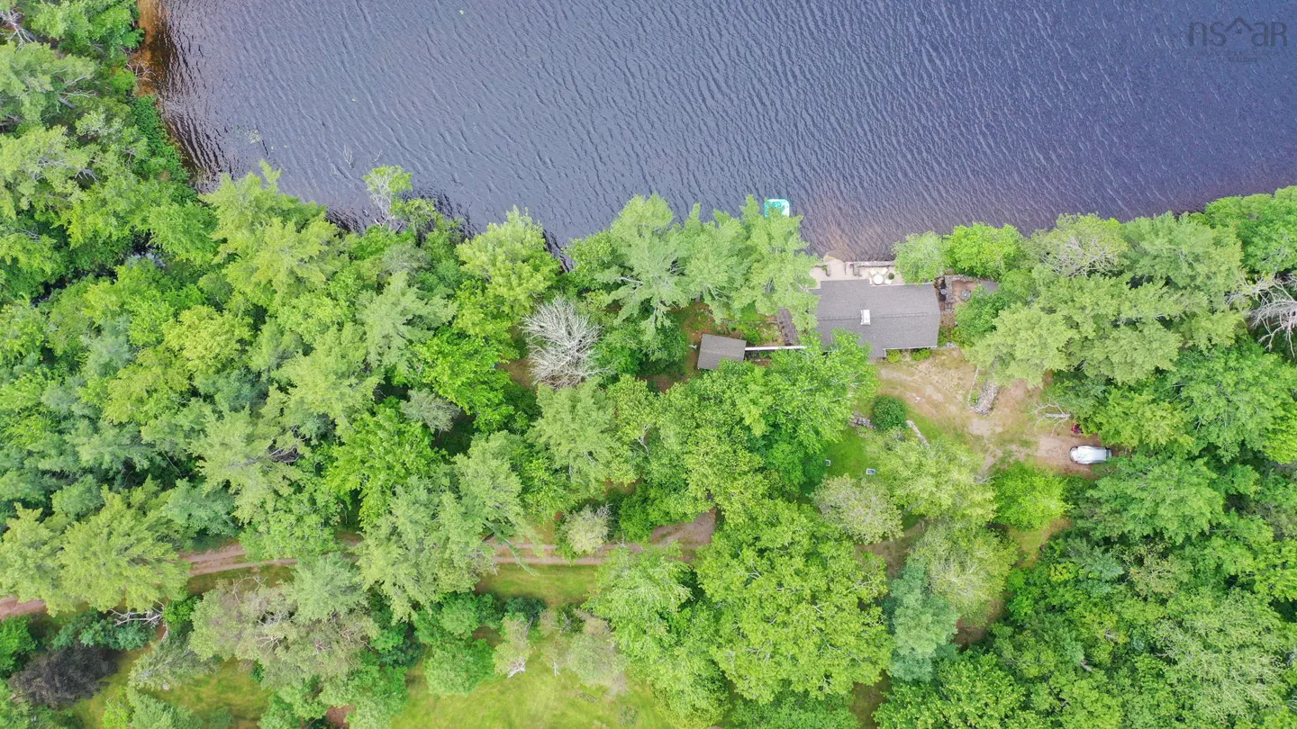 Aerial view of a lake house surrounded by green trees, next to a dark blue lake.