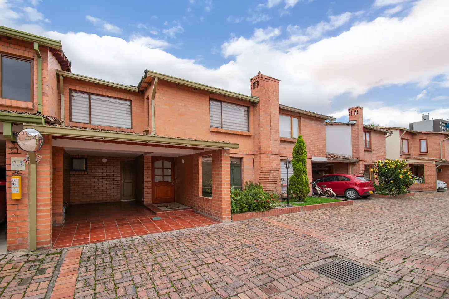 Exterior view of red brick townhouses with carports and brick-paved driveway under a blue sky with white clouds.