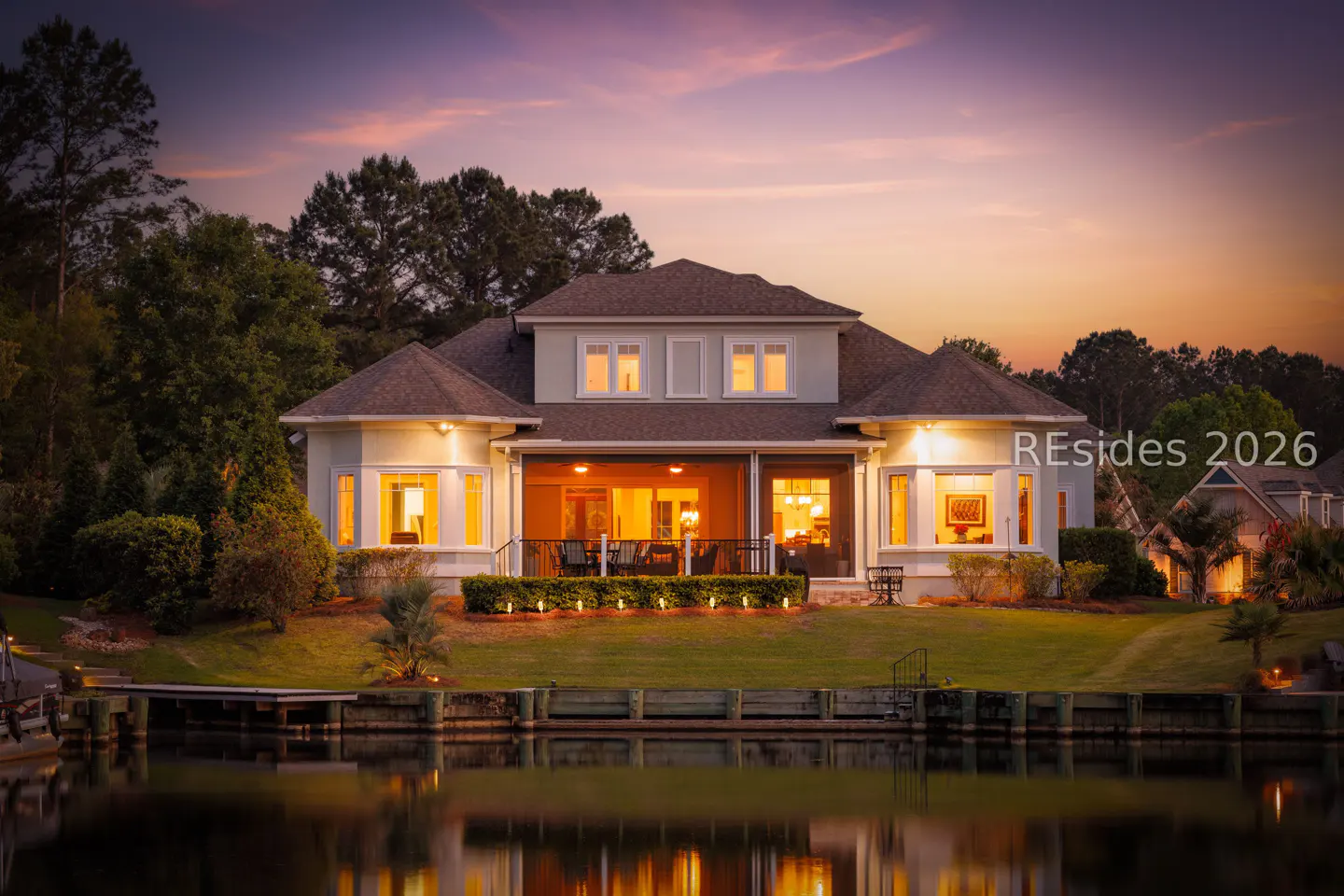 Two-story house with a brown roof, light green siding, and a waterfront view at sunset.