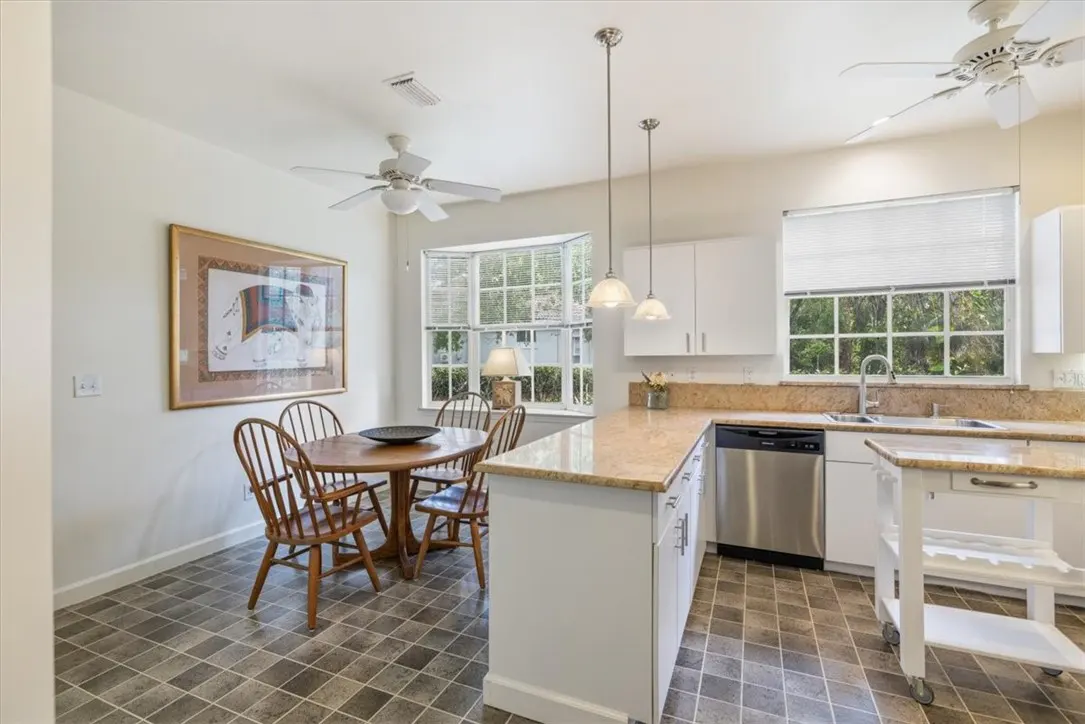 Bright kitchen with white cabinets, granite countertops, stainless steel appliances, and a round wooden dining table with four chairs.