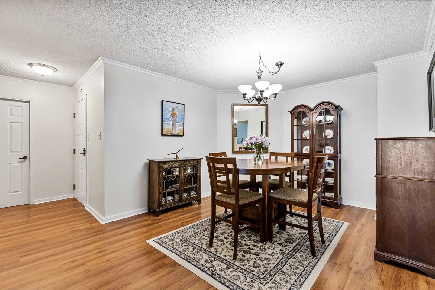 A dining room with a round wooden table, four chairs, and a patterned rug on a wood floor.