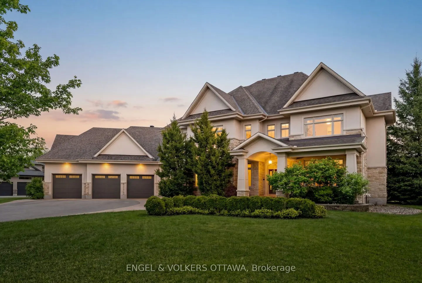 A large, beige two-story house with a three-car garage and green lawn at dusk.