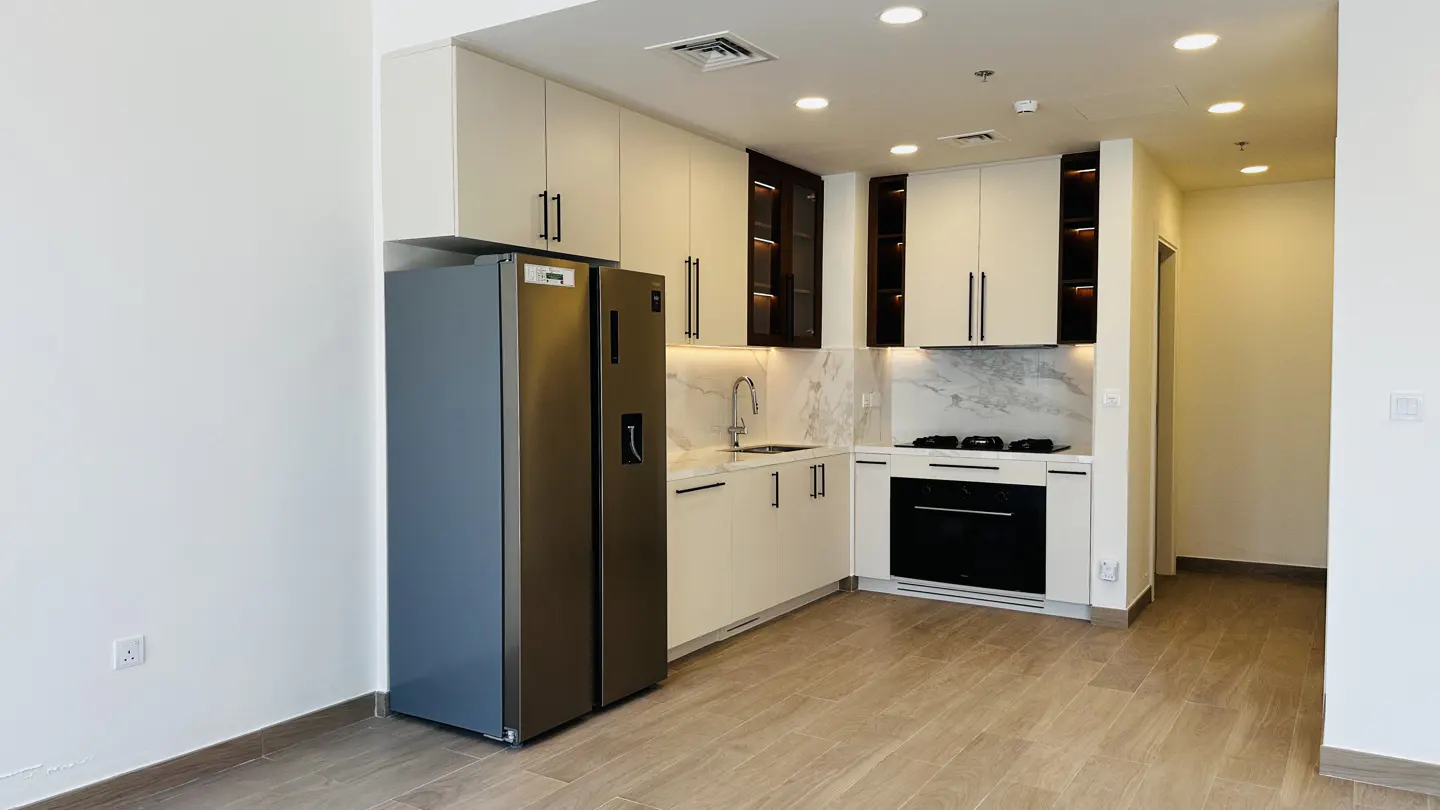 A modern kitchen with white cabinets, marble backsplash, stainless steel appliances, and light wood-look flooring.
