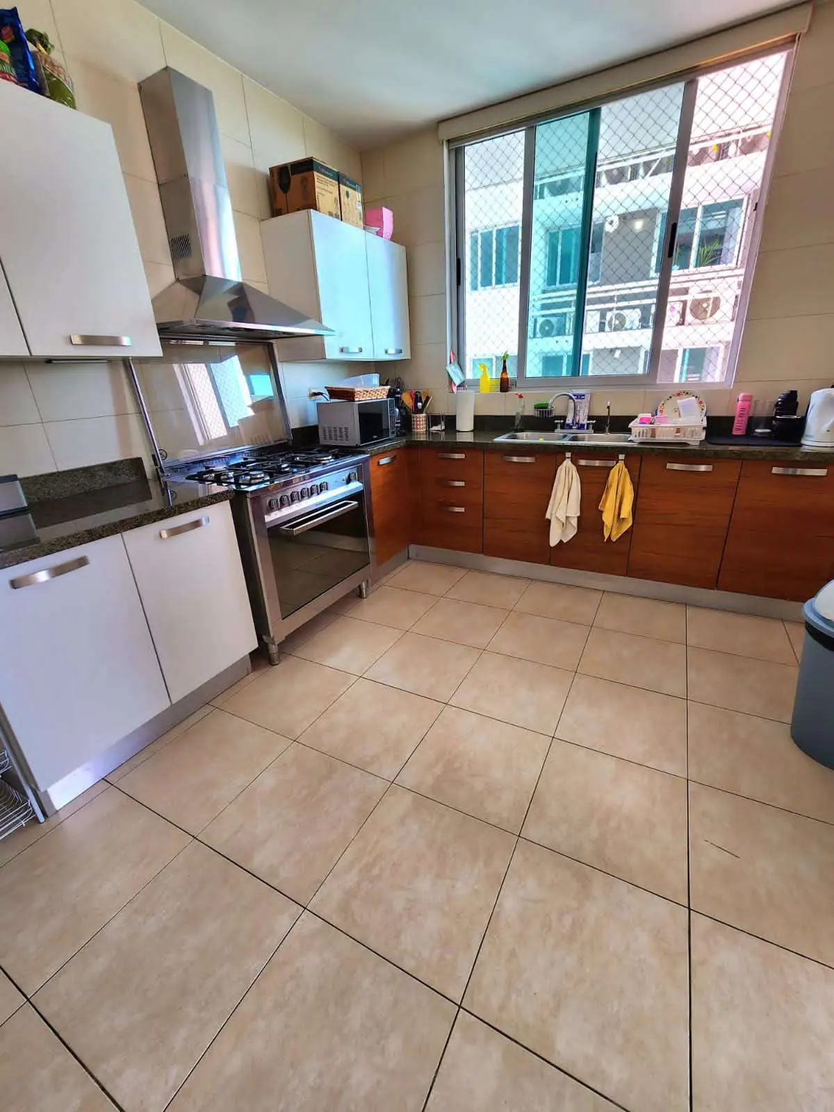 A bright kitchen with white and wood cabinets, stainless steel appliances, and a large window.