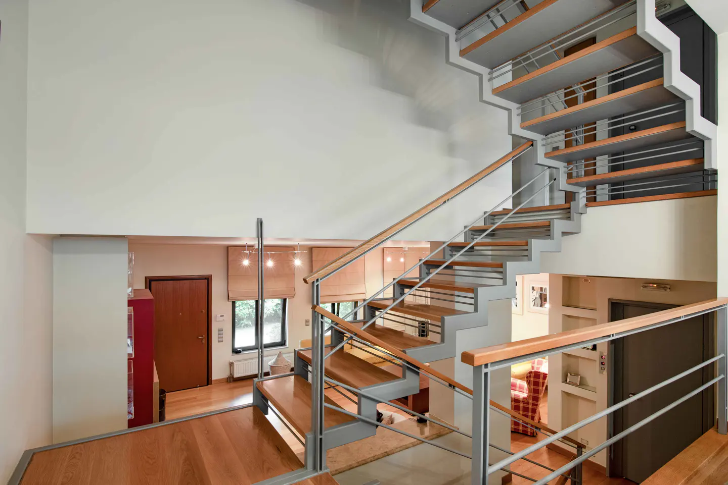 Interior view of a modern home featuring a wooden staircase with metal railings, leading to an upper level with a white wall.