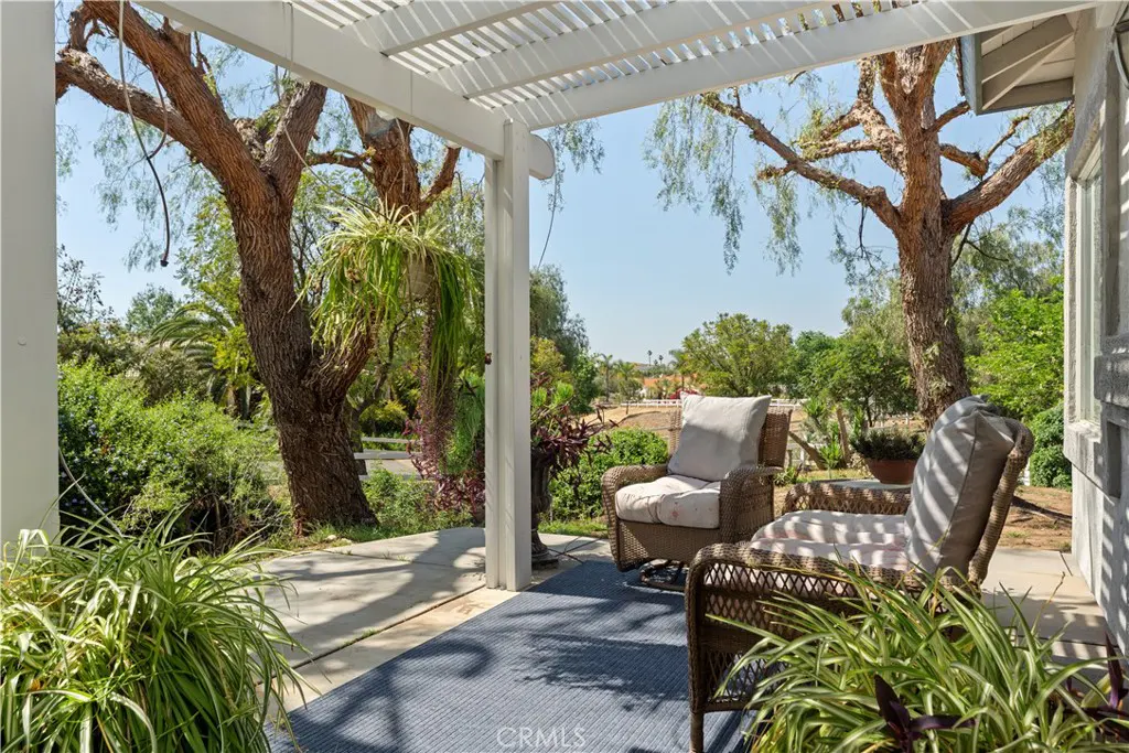 Covered patio with two wicker chairs and a blue rug, overlooking a lush green landscape.