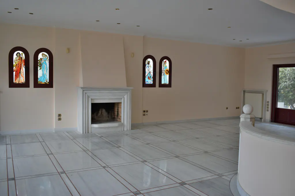 An empty living room with marble floors, a fireplace, and stained glass windows. The walls are light peach.