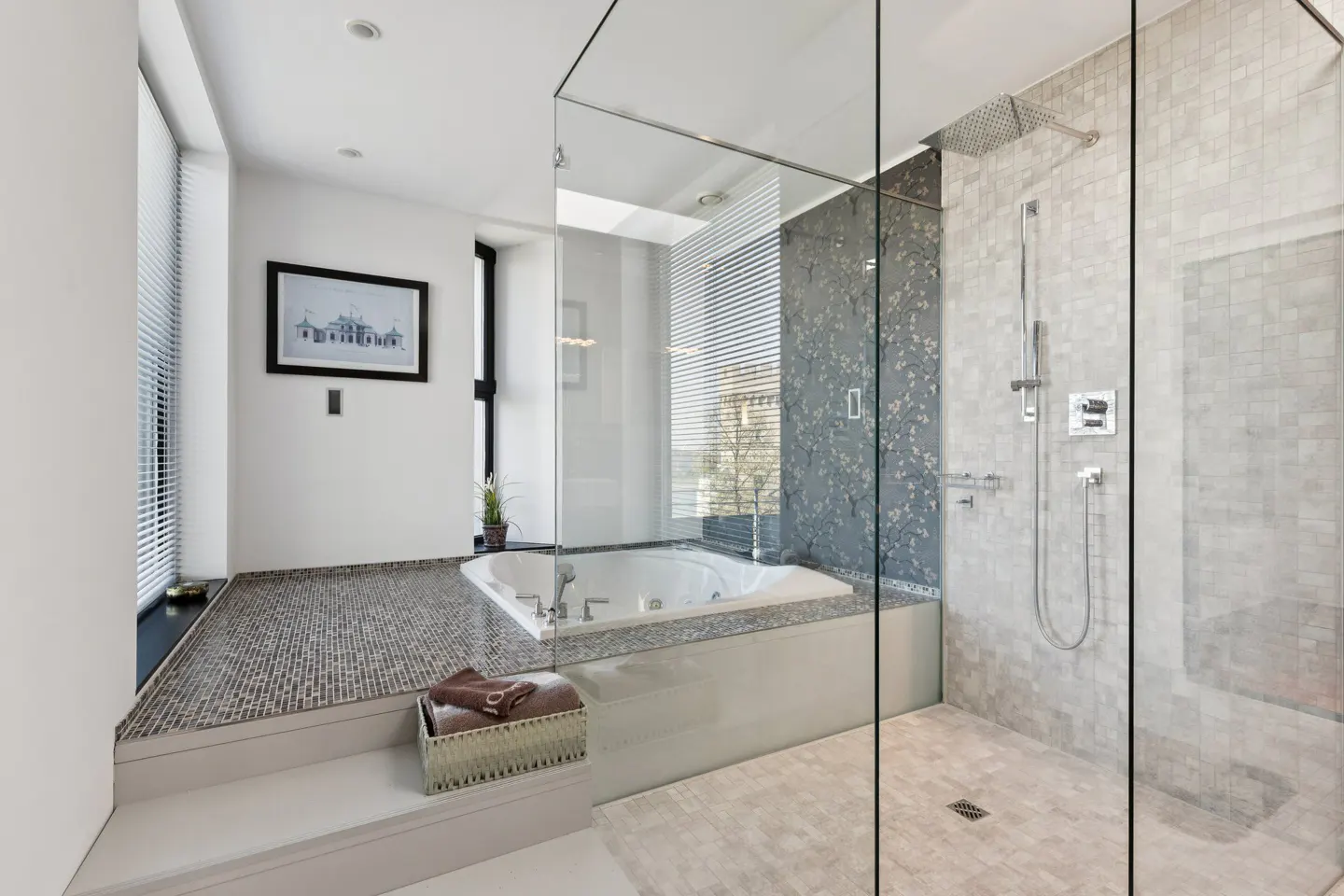 Modern bathroom with a glass-enclosed shower, a white jacuzzi tub, and gray mosaic tile flooring. A basket of towels sits on the step.