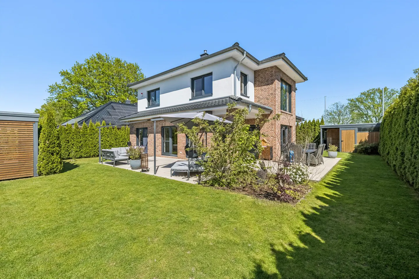 Two-story house with brick and white siding, a patio with outdoor furniture, and a green lawn on a sunny day.
