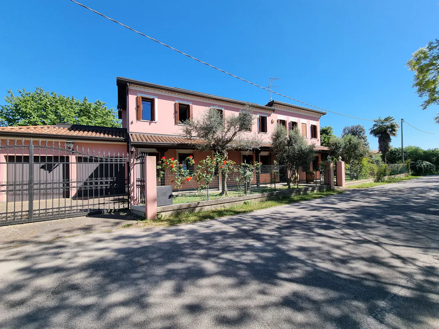 Two-story pink house with brown shutters and a black iron gate on a sunny day.