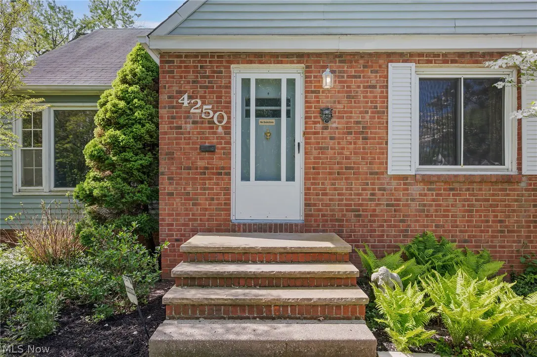 Exterior of a brick house with white door and shutters, and stone steps leading to the entrance. Address number 4250 is visible.