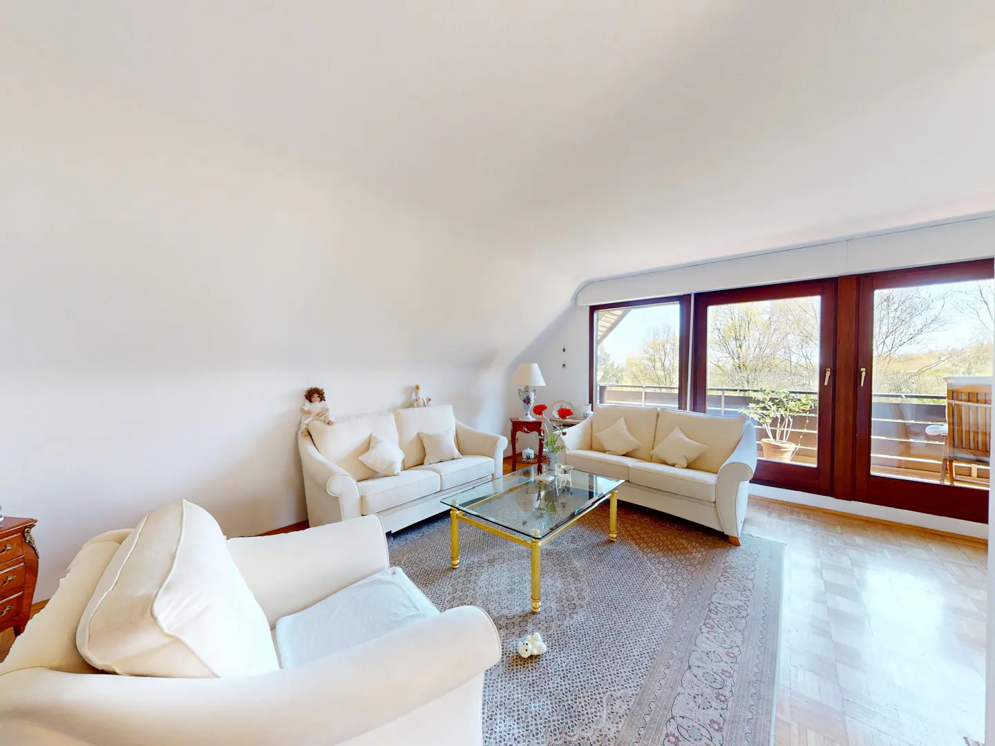 Bright living room with white sofas, glass coffee table, and large windows leading to a balcony.