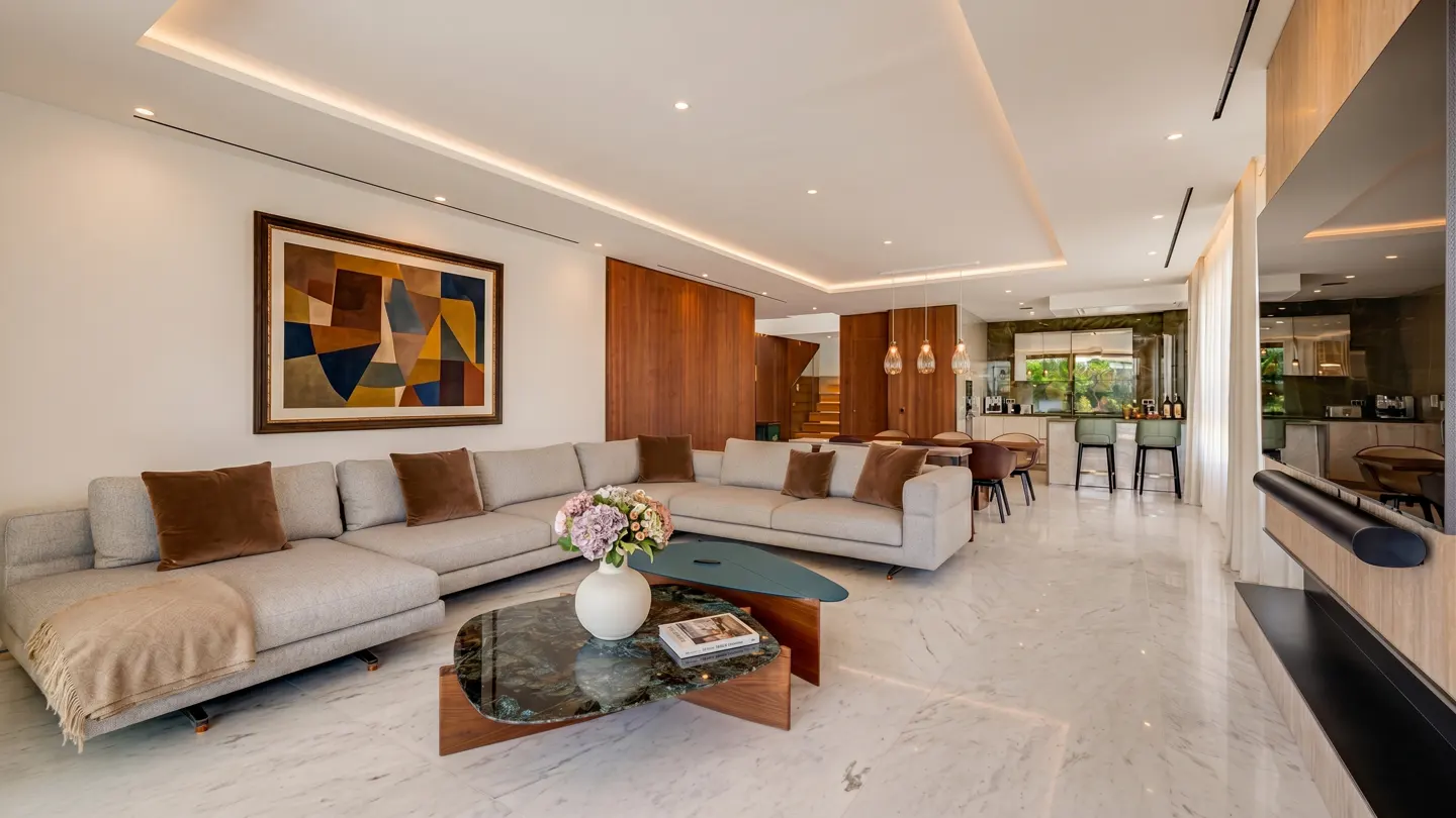 Bright, open-concept living room with marble floors, a gray sectional sofa with brown pillows, and a unique coffee table with flowers. An abstract painting hangs on the wall.