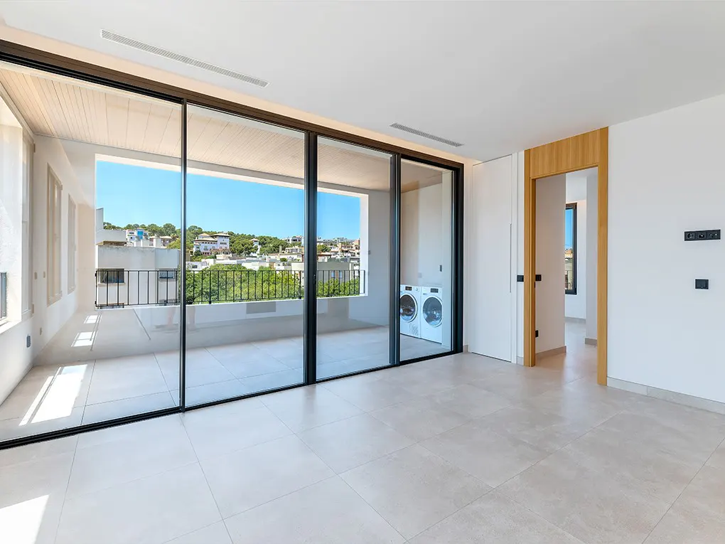 Bright, modern room with large sliding glass doors to a balcony with city views. White washer and dryer visible. Neutral tile floor.
