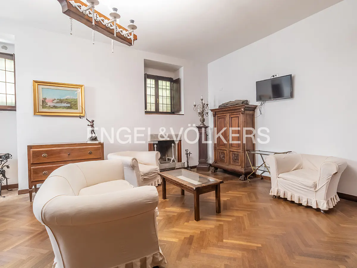 Living room with herringbone wood floors, white walls, fireplace, and white armchairs. A wooden dresser and TV are also visible.